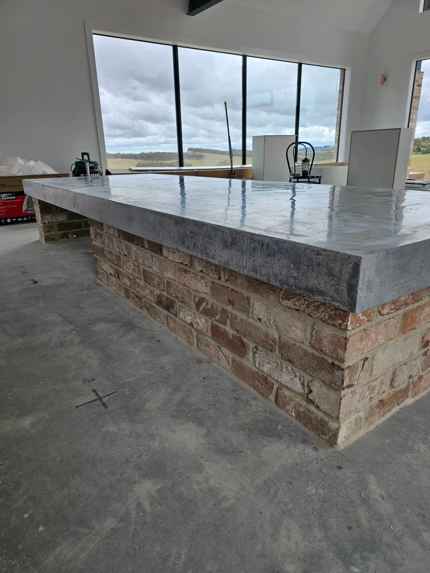 A honed concrete island bench with rolling green hills through the window behind it